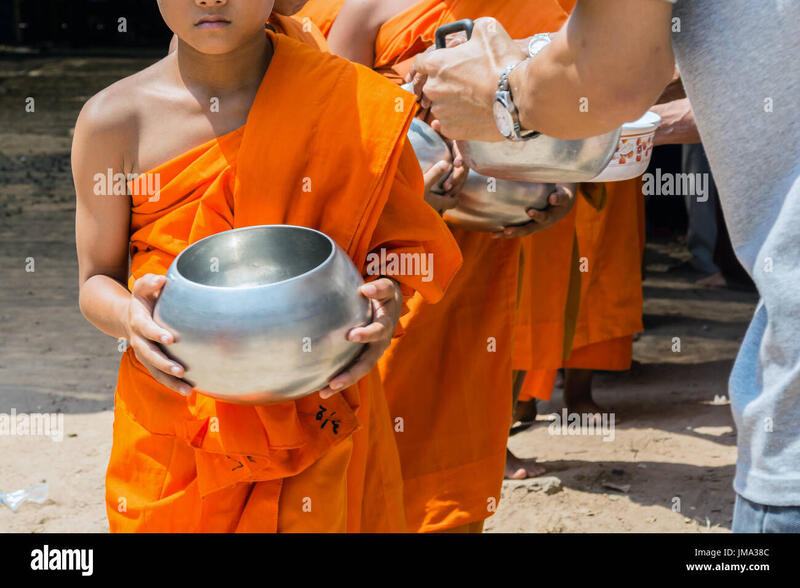 Young Buddhist monks in orange robes receiving alms in metal bowls during a traditional morning ceremony