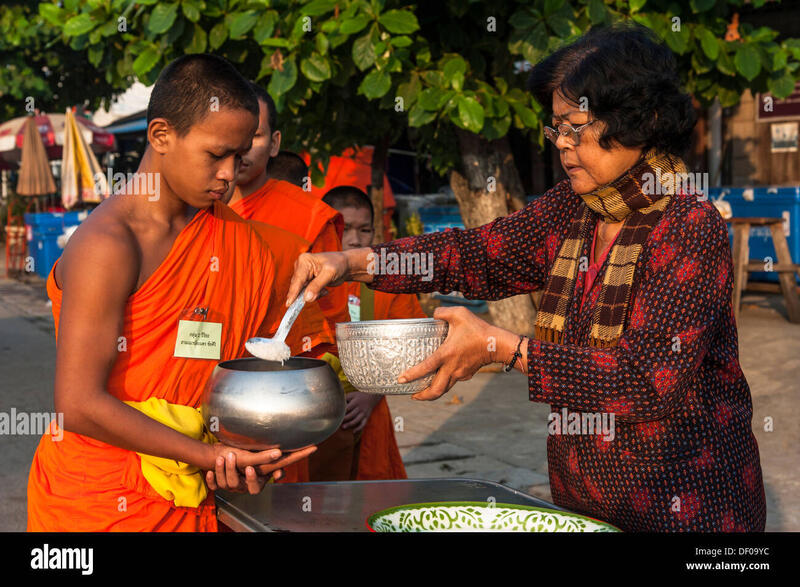 A Thai woman offering rice to a young Buddhist monk during the morning alms round, a traditional practice in Thai Buddhist culture